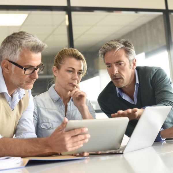 3 Geschäftsleute/ eine Frau und zwei Männer schauen gemeinsam auf ein Tablet und einen Laptop