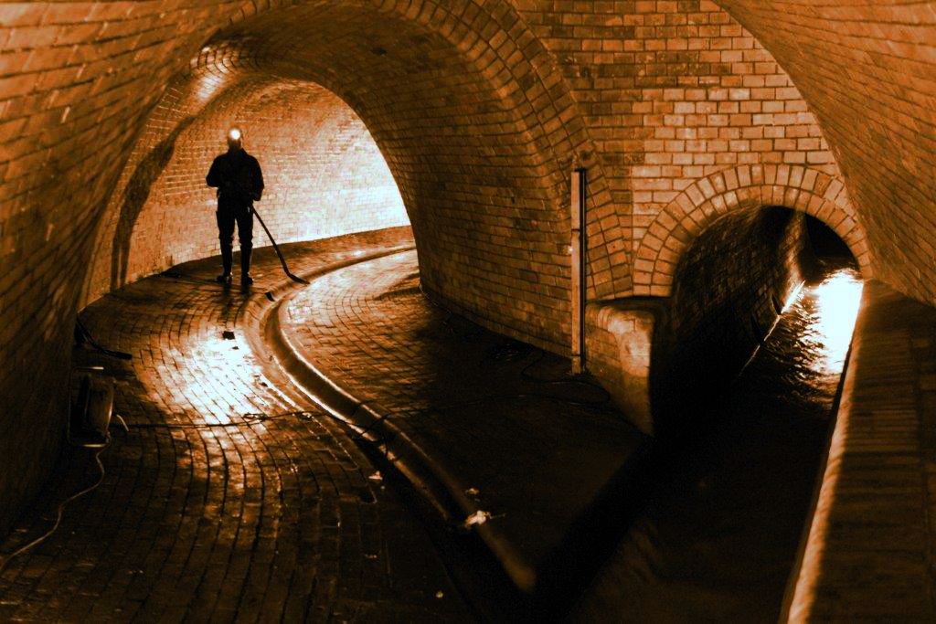 Person mit Stirnlampe in unterirdischer Kanalisation