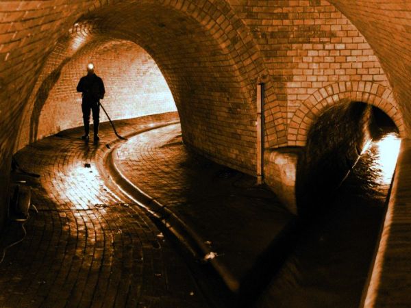 Person mit Stirnlampe in unterirdischer Kanalisation