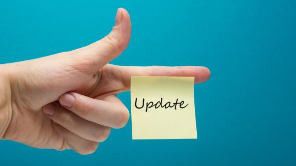 Eine linke Hand mit ausgestrecktem Zeigefinger, an dem ein gelber quartratischer unbeschrifteter Klebezettel klebt vor blauem Hintergrund.