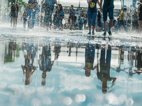 Spiegelung der Menge fröhlicher Menschen beim Stadtbrunnen. Heller, sonniger Frühlings- oder Sommertag
