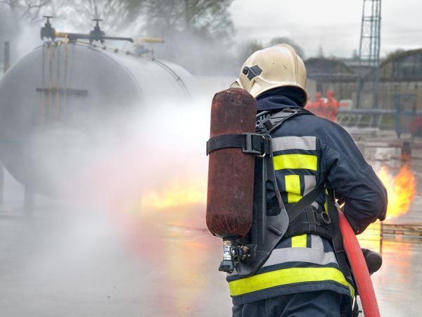 Feuerwehrperson löscht ein Feuer bei einem Tankbehälter
