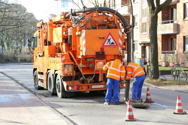 Tank-LKW für Kanalreinigung wird von 2 Arbeitern bedient, Der eine hält das Absaugrohr fest.