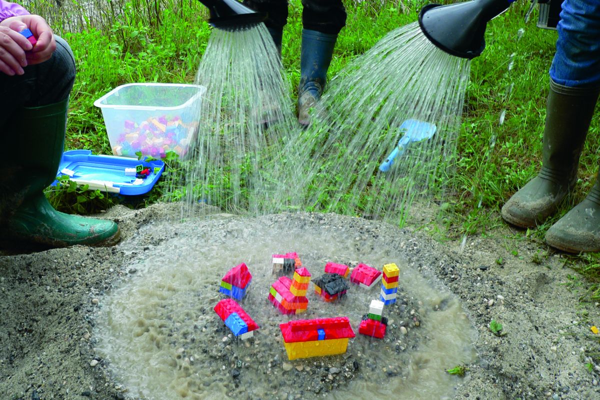Legosteine werden von Menschen in Gummistiefeln mit Gießkannen begossen
