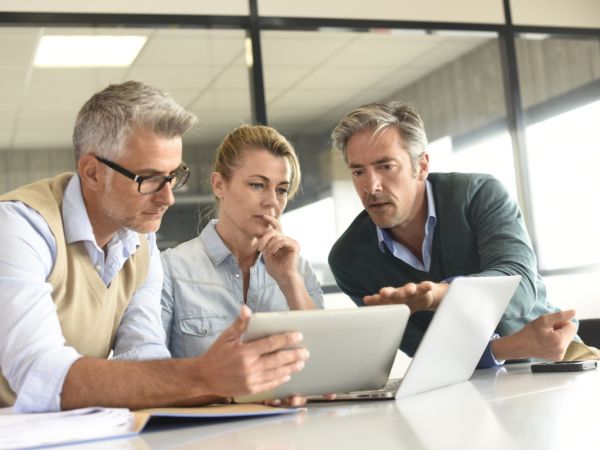 3 Geschäftsleute/ eine Frau und zwei Männer schauen gemeinsam auf ein Tablet und einen Laptop