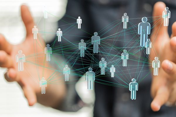 Abstrakte 3d Abbildung von vernetzten Menschen, vernetzt mit verschiedenfarbigen Netzfäden und unterschiedlich stark vernetzt. Im Hintergrund ein Mensch, nur verschwommen zu sehen ist, der dieses Netzwerk in seinen senkrecht geöffneten Händen hält.