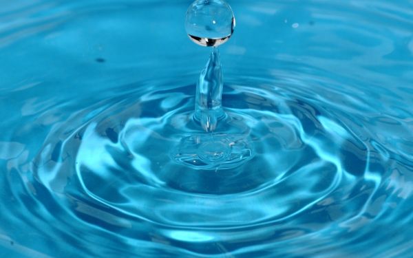 Ein Wassertropfen fällt in klares, blaues Wasser