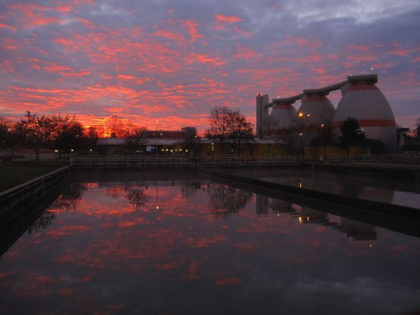 Abendröte über den Belebungsbecken einer Kläranlage. Im Hintergrund sind drei Faulbehälter zu sehen