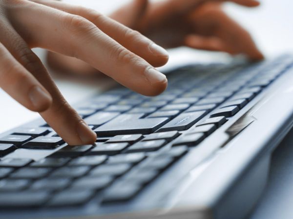 Eine Person bedient zweihändig eine Computertastatur, wobei die linke Hand und der größte Teil der Tastatur undeutlich zu sehen ist und die rechte Hand im Vordergrund deutlich.