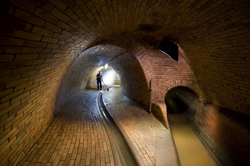 Ein Kanalarbeiter mit einem Besen verrichtet eine Bestandspflegetätigkeit in der Kanalisation.