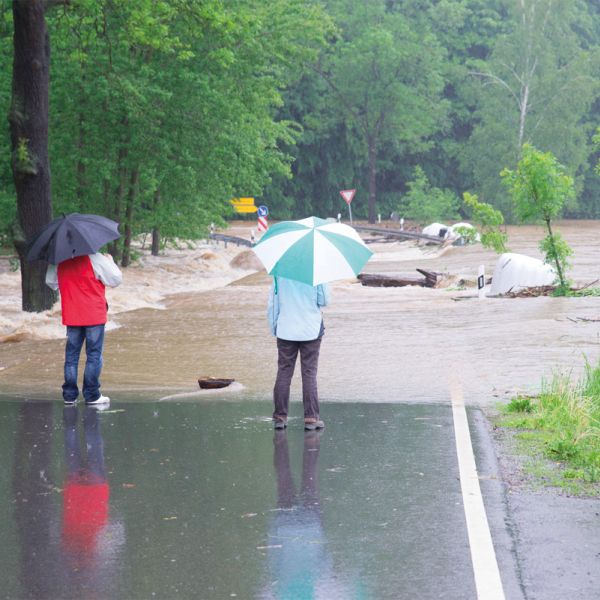 2 Passanten stehen auf der überfluteten Straße bei Regen und Hochwasser