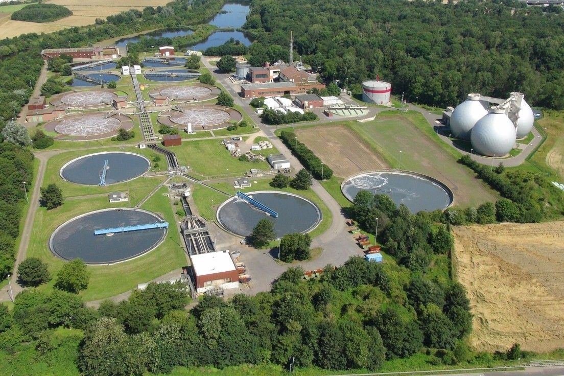 Drohnenbild der Kläranlage Düren-Merken, umgeben von Getreidefeldern, Wald und Teichen, in der Nähe einer Siedlung.