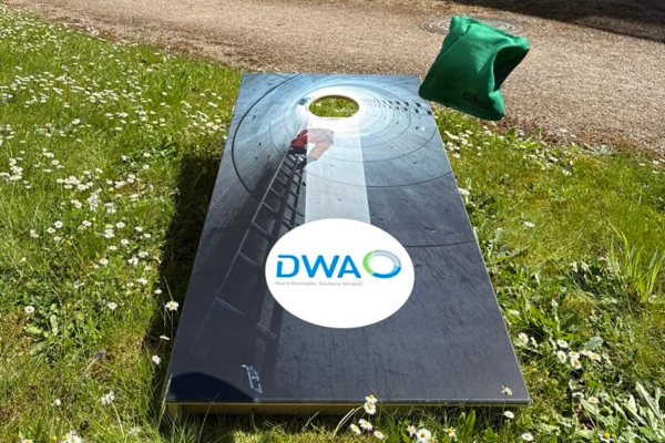 Ein Säckchen fliegt gerade auf ein Cornhole-Spiel, dass auf der grünen Wiese steht.