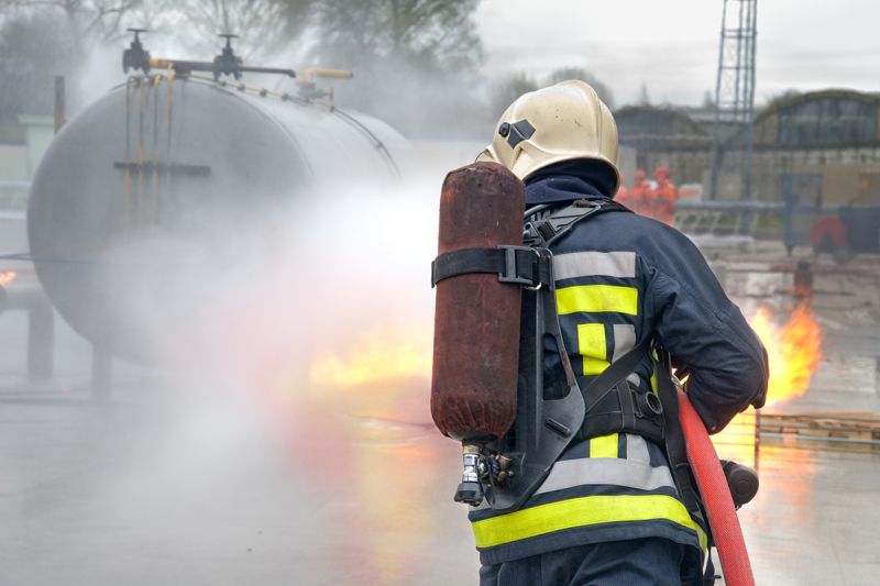 Feuerwehrperson löscht ein Feuer bei einem Tankbehälter
