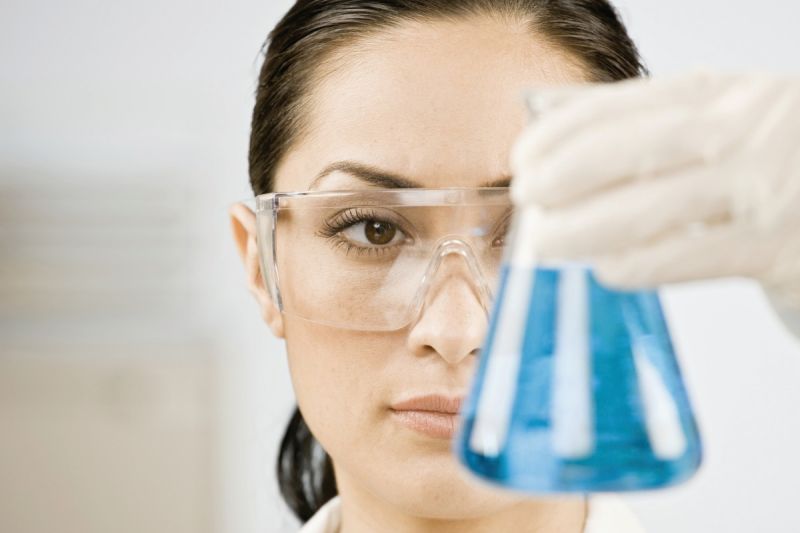 Eine Forscherin schaut in ein Laborbecherglas mit blauer Flüssigkeit