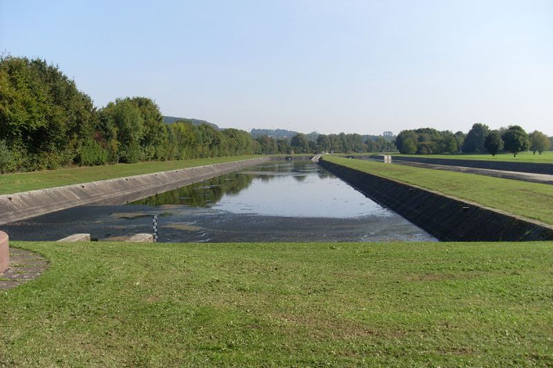 Blick in zwei fast leere Regenrückhaltebecken umgeben von Gras und Bäumen.