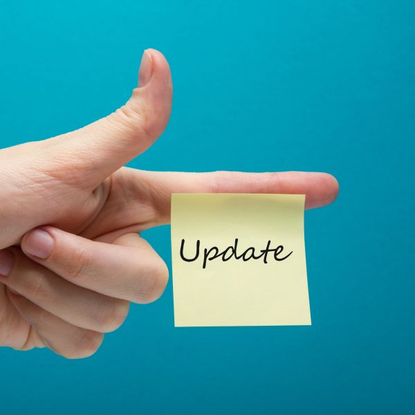 Eine linke Hand mit ausgestrecktem Zeigefinger, an dem ein gelber quartratischer unbeschrifteter Klebezettel klebt vor blauem Hintergrund.