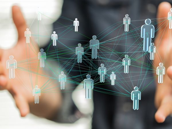 Abstrakte 3d Abbildung von vernetzten Menschen, vernetzt mit verschiedenfarbigen Netzfäden und unterschiedlich stark vernetzt. Im Hintergrund ein Mensch, nur verschwommen zu sehen ist, der dieses Netzwerk in seinen senkrecht geöffneten Händen hält.