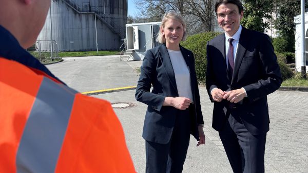 Lisa Bross und Uli Paetzel stehen vor Faulturm auf einer Kläranlage an einem sonnigen Tag