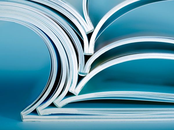 Ein Stapel mit 7 mittig aufgeklappten Magazinen, die mittig übereinanderliegen. Mit weißen und blauen Seiten vor blauem Hintergrund.