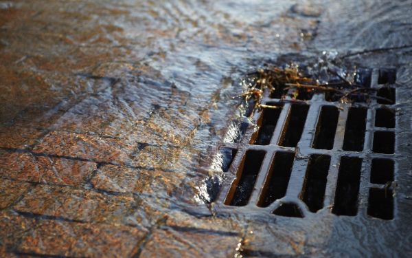 Abwasser läuft in einen vergitterterten Einlaufschacht für Strassenabwässer am Rand einer gepflasterten Straße.