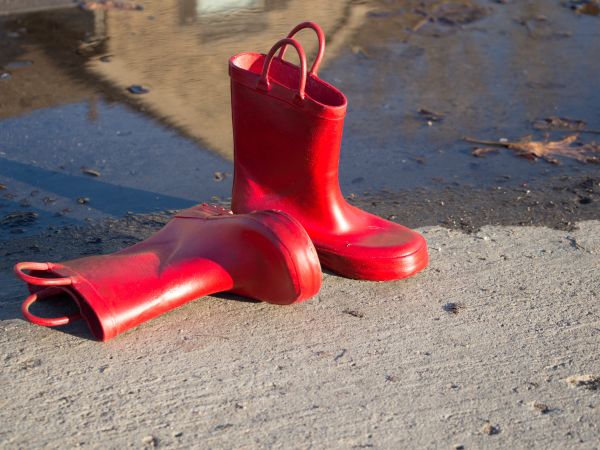 ein liegender und ein stehender Gummistiefel in einem leuchtenden Rot vor einer Pfütze