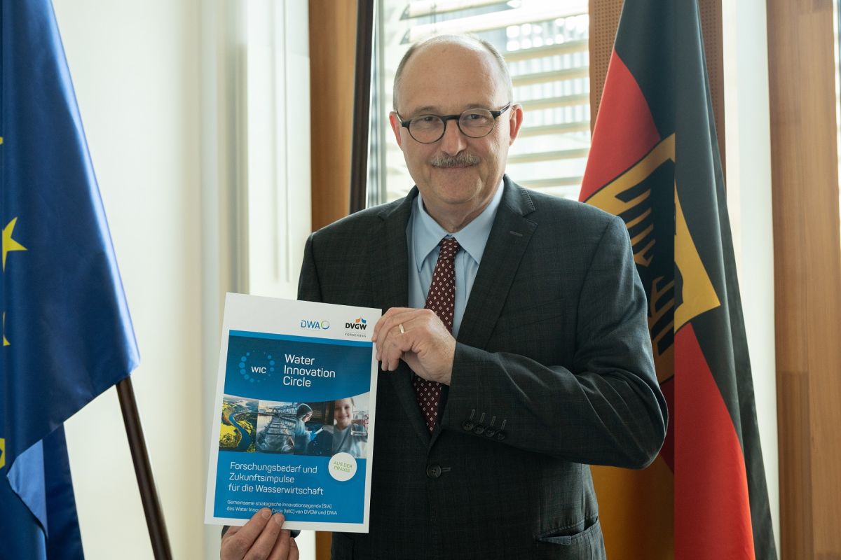 Staatssekretär Meister hält die Broschüre Forschungsbedarf und Zukunftsimpulse für die Wasserwirtschaft in die Kamera