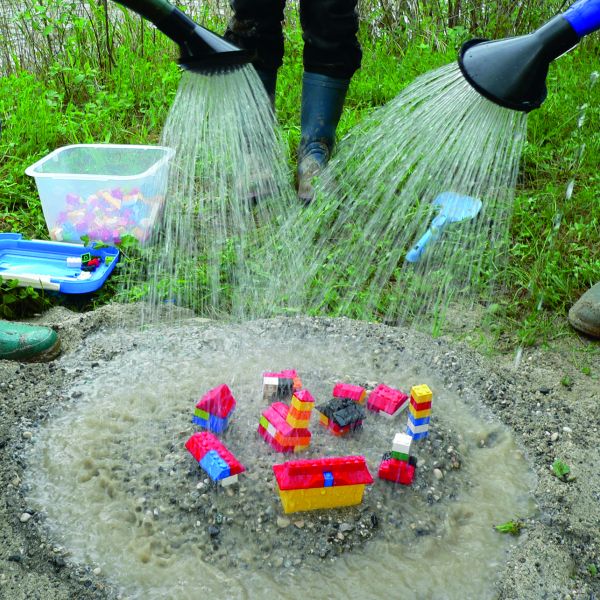 Legosteine werden von Menschen in Gummistiefeln mit Gießkannen begossen