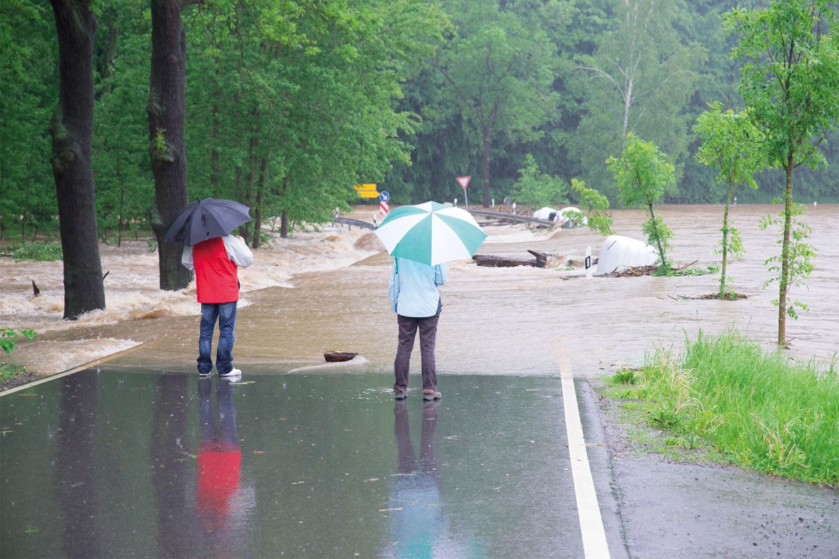 2 Passanten stehen auf der überfluteten Straße bei Regen und Hochwasser