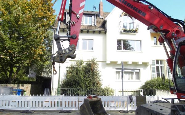 Baggereinsatz an einer Kanal-Baustelle in einem Bonner Wohngebiet. Baustelle ist mit Absperrgitter und Bake gesichert.
