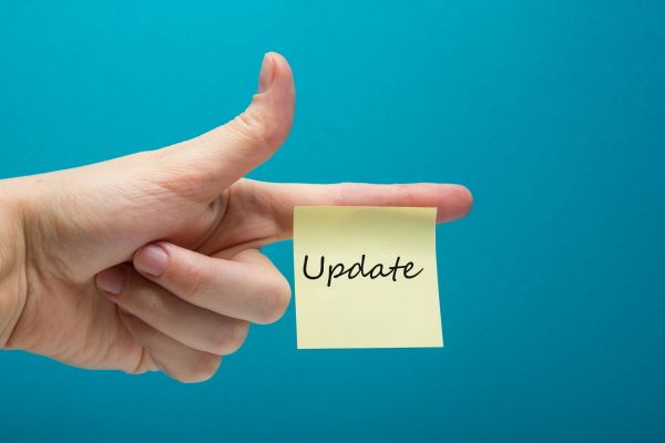 Eine linke Hand mit ausgestrecktem Zeigefinger, an dem ein gelber quartratischer unbeschrifteter Klebezettel klebt vor blauem Hintergrund.