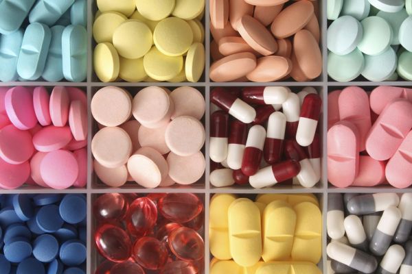 Verschiedenfarbige Tabletten und Kapseln in einer Kunststoffortnungsbox mit 12 gleichgroßen Fächern.