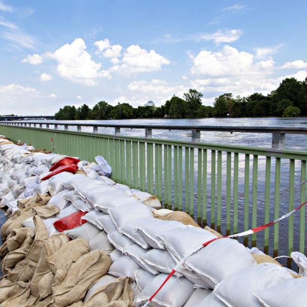 Hochwasser der Elbe im Juni 2013 in Magdeburg. Als Schutzmaßnahme sind ca. 2 mtr breite und 1 mtr hohe Sandsackdämme am grünen Ufergeländer gestabelt. Der Uferweg ist leicht überschwemmt. Leute gehen oder fahren mit dem Fahrrad durchs Hochwasser.