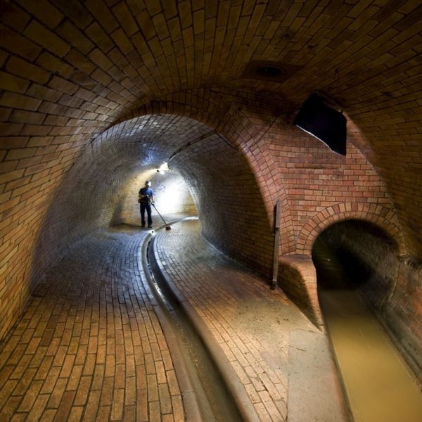 Ein Kanalarbeiter mit einem Besen verrichtet eine Bestandspflegetätigkeit in der Kanalisation.