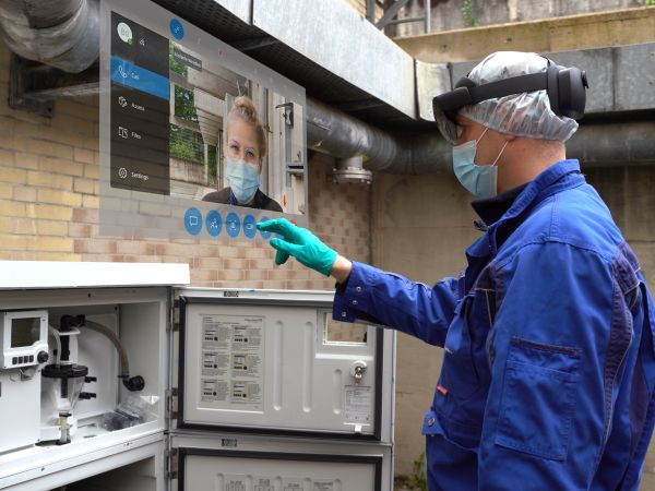 Mitarbeiter mit der Hololensbrille steht vor dem Probenahmeschrank . Er tippt auf einen  Bildschirm, dass die Hololens vor seinem Gesicht  projiziert