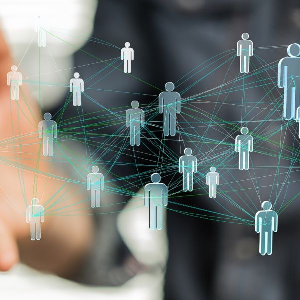 Abstrakte 3d Abbildung von vernetzten Menschen, vernetzt mit verschiedenfarbigen Netzfäden und unterschiedlich stark vernetzt. Im Hintergrund ein Mensch, nur verschwommen zu sehen ist, der dieses Netzwerk in seinen senkrecht geöffneten Händen hält.